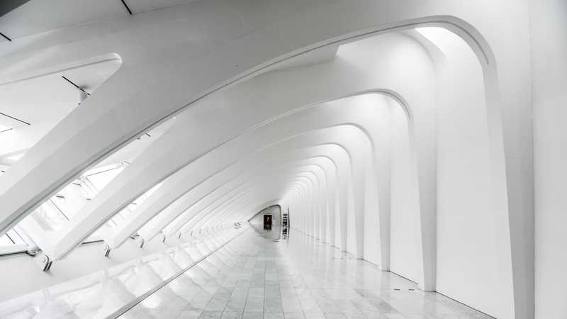 A white, rounded, triangular, futuristic looking room where arches span the ceiling.